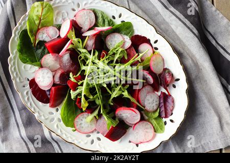 Salat mit Rote Bete, Rucola, Rettich, Spinat auf grauem Hintergrund, Draufsicht. Gesundes Essen. Frühlingssalat Stockfoto