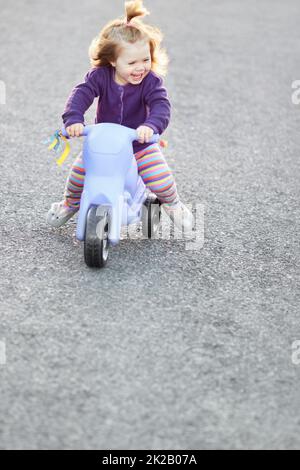 Spaß auf ihrem Dreirad. Ein süßes Mädchen, das draußen auf der Straße auf ihrem Dreirad reitet. Stockfoto
