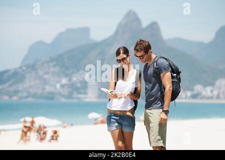 Sich im Paradies zurechtzufinden. Aufnahme eines jungen Paares, das auf eine Karte schaut, während es am Strand steht. Stockfoto