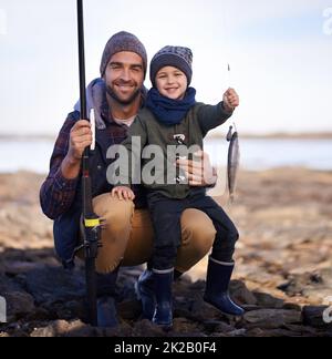 Ein Punkt für mich keiner für Vater. Porträt eines niedlichen kleinen Jungen, der den Fisch hält, den er mit seinem Vater gefangen hat. Stockfoto