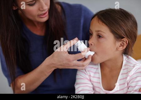 Atmen Sie ein, Honig. Aufnahme einer fürsorglichen Mutter, die ihrer Tochter zu Hause eine Asthmapumpe gab. Stockfoto