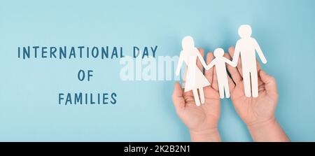 Internationaler Tag der Familien, Eltern mit einem Kind, das die Hände hält, Papier ausgeschnitten, blauer Hintergrund, Beziehung Stockfoto