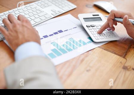 Addieren der Zahlen. Eine Aufnahme eines Geschäftsmanns, der einen Rechner an seinem Schreibtisch benutzt. Stockfoto