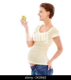 Gesunde Ernährung für das Baby. Eine Schwangere, die einen knusprigen grünen Apfel betrachtet, während sie auf weißem Hintergrund isoliert ist. Stockfoto