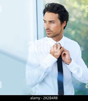 Vorbereitung auf ein Meeting. Ein hübscher junger Geschäftsmann, der seine Krawatte anpasst. Stockfoto