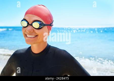 Training, um ein Lebensretter zu sein. Eine junge Frau, die im Winter am Strand in einem vollteiligen Neoprenanzug und Schwimmkleidung trainiert. Stockfoto