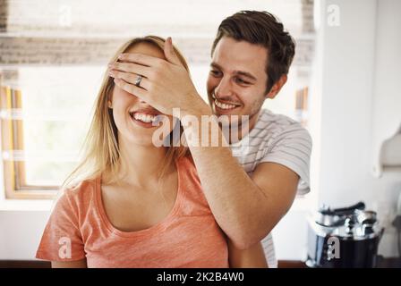 Liebe ist nicht etwas, was man sieht, es ist etwas, das man fühlt. Aufnahme eines jungen Mannes, der zu Hause spielerisch die Augen seiner Freundinnen bedeckt. Stockfoto