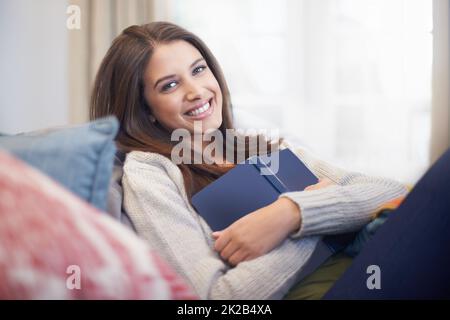 Eine junge Frau, die mit einem Buch auf der Couch liegt. Entspannen mit ihrem Lieblingsbuch. Stockfoto