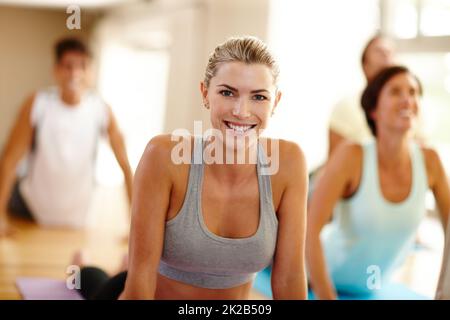 Besuchen Sie uns für eine gezielte Fitness. Porträt einer schönen Frau, die in einem Yoga-Kurs Übungen macht. Stockfoto