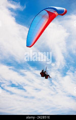 Zwei in einem. Blick aus der unteren Perspektive auf zwei Personen, die hoch oben beim Tandem-Paragliding sind. Stockfoto