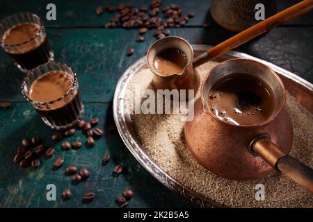 Von oben aus Metall-Cezves gefüllt mit frisch gebrühtem aromatischem heißen orientalischen Kaffee auf Sand, der mit Gläsern auf den Tisch gelegt wird Stockfoto