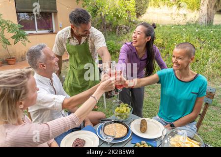 Eine Gruppe von glücklichen Freunden toasten und genießen mit einem schönen Lächeln um den Tisch im Haus Terrasse Diner. Stockfoto
