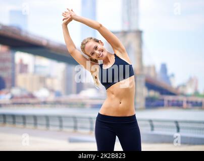 Übung auf der Seite. Porträt einer schönen Frau, die sich vor ihrem Lauf in der Stadt ausdehnt. Stockfoto