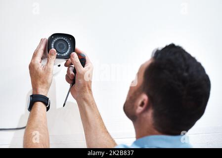 Könnt ihr mich da unten sehen? Aufnahme eines reifen Mannes, der eine Sicherheitskamera auf einem Gebäude installiert. Stockfoto