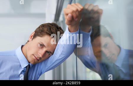 HES spürt den Druck. Ein müder junger Geschäftsmann, der sich an einer Glaswand lehnt. Stockfoto