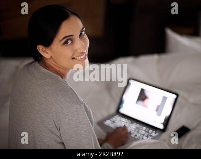 Ich hole einen alten Freund ein. Eine junge Frau, die im Bett an ihrem Laptop arbeitet. Stockfoto