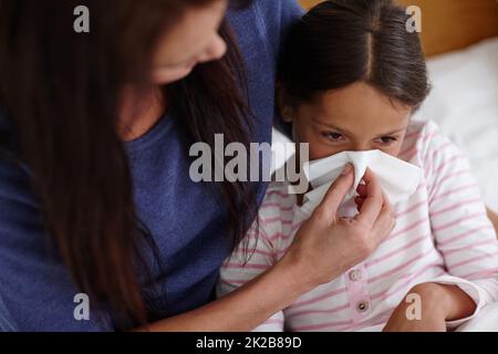 Wenn eine Erkältung einschlägt Aufnahme einer Mutter, die ihrer kranken Tochter hilft, sich die Nase zu blasen. Stockfoto