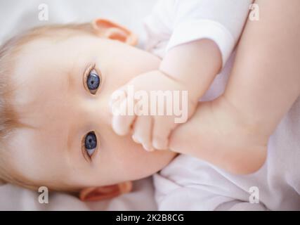 Diese Dinge machen ziemlich viel Spaß. Nahaufnahme eines entzückenden Babys, das sich hinlegt und mit seinen Füßen spielt. Stockfoto