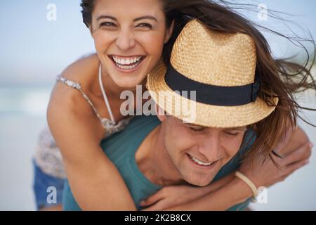 Sie haben immer Spaß zusammen. Ein junges Paar Huckepack am Strand. Stockfoto