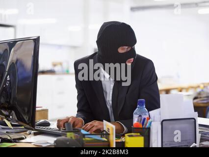 Machen Sie einige illegale Aktivitäten ... Aufnahme eines Hackers in schwarzer Maske, der einen Computer hackt. Stockfoto