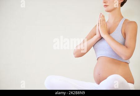 Halten Sie ihren Körper und Geist in guter Form für das Baby. Eine junge, schwanger sitzende Frau in einer Yoga-Pose - abgeschnitten. Stockfoto