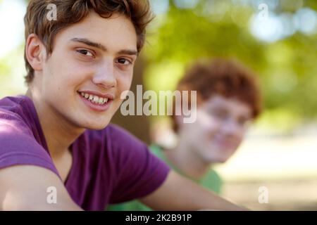 Genießen Sie die frische Luft. Porträt von zwei Jungen im Teenageralter, die an einem sonnigen Tag in einem Park sitzen. Stockfoto