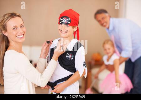 Dress up ist die Spezialität von Mums. Porträt einer Mutter, die an halloween einen Schnurrbart auf das Gesicht ihres Sohnes malt, wobei Vater und Schwester im Hintergrund spielen. Stockfoto