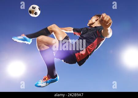 Hes hat Spiel. Aufnahme eines jungen Fußballers, der mitten in der Luft einen Ball tritt. Stockfoto