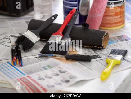 Die Werkzeuge des Handels. Beschnittene Nahaufnahme von Pinsel und Farbdosen auf der Zeitung. Stockfoto