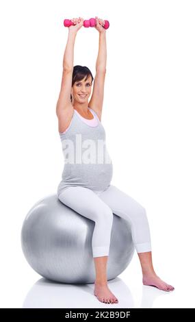 In Form bleiben, bis zu ihrem letzten Trimester. Eine Schwangere lächelt mit einem Pilates Ball, während sie auf Weiß isoliert ist. Stockfoto