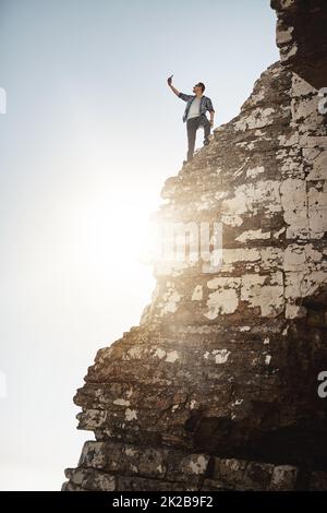 Aufnahme eines Fotos aus großer Höhe. Aufnahme eines jungen Mannes, der am Rand einer Bergklippe fotografiert. Stockfoto