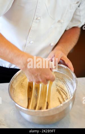 Gehen Sie nicht zu weit. Schuss eines Bäckers, der Teig in einer Schüssel knetet. Stockfoto