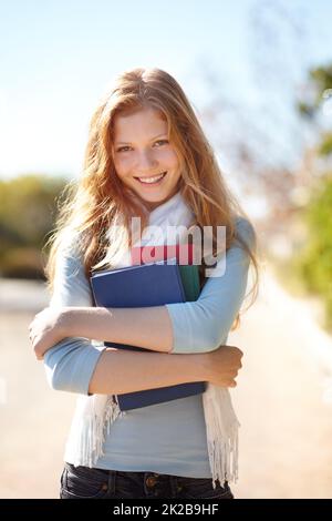 Sie liebt ihre Bücher. Porträt eines jungen Mädchens, das ihre Schulbücher nahe an ihre Brust hält. Stockfoto