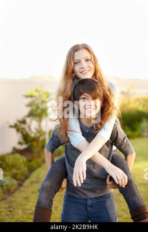 Er wird immer für sie da sein. Porträt eines Jungen, der seiner Schwester im Garten einen Huckepack gab. Stockfoto