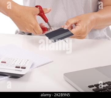 Ihre Einkäufe sind zu umfangreich. Nahaufnahme einer Frau, die ihre Kreditkarte mit einem Laptop und einem Rechner vor sich schneidet. Stockfoto