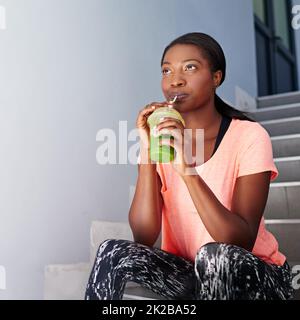 Gedanken an Fitness. Aufnahme einer attraktiven jungen Frau, die beim Training im Freien Saft trinkt. Stockfoto