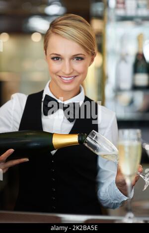 Eleganz, Stil und Anmut. Porträt einer Bardame, die Champagner für eine besondere Feier ausgießt. Stockfoto