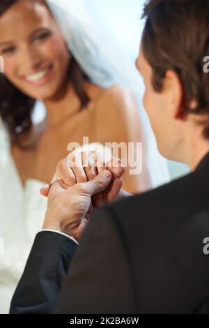 Versprechen zu machen, zu lieben und zu ehren. Beschnittene Ansicht eines Bräutigams, der seine neue Brauthand hält. Stockfoto