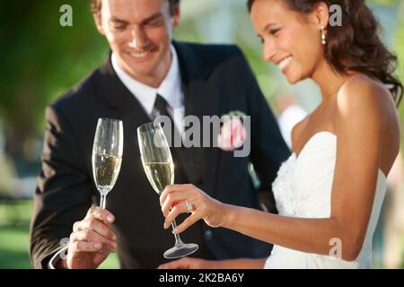 Heres zu unserer Romantik. Beschnittene Ansicht einer jungen Braut und eines Bräutigams, die zusammen stehen und ihre Ehe toasten. Stockfoto