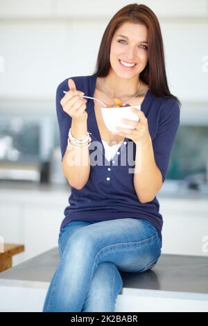 Gönnen Sie sich einen gesunden Snack. Porträt einer lächelnden jungen Frau, die mittags einen gesunden Obstsalat isst. Stockfoto