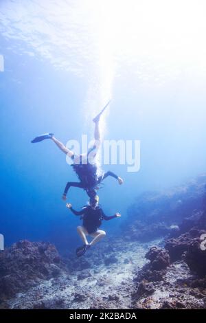 Unterwasserabenteuer. Zwei schwimmende Taucher, die Kopf an Kopf und auf dem Kopf unter Wasser herumtörneln - Copyspace. Stockfoto