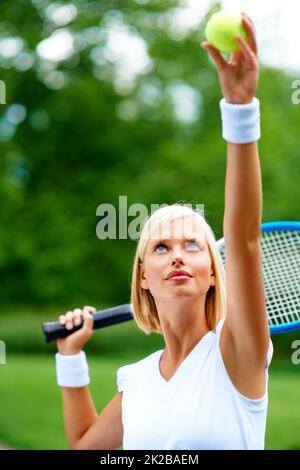 Lass das Spiel beginnen.... Eine junge Tennisspielerin, die sich bereit gemacht hat, dem Ball zu dienen. Stockfoto