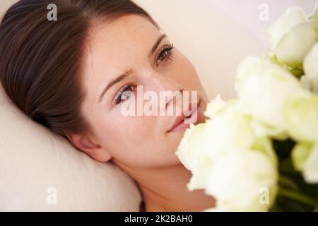 Sich verlieben. Eine schöne junge Frau, die sich hinlegt und einen Strauß weißer Rosen an ihre Brust hält. Stockfoto