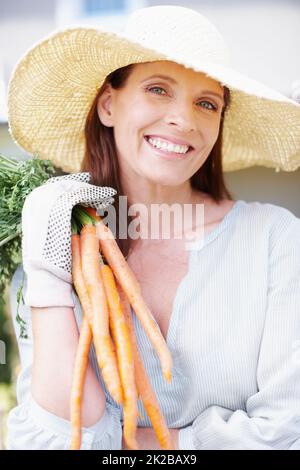 Ein Haufen Güte. Porträt einer lächelnden Frau, die ein paar Karotten hochhält. Stockfoto