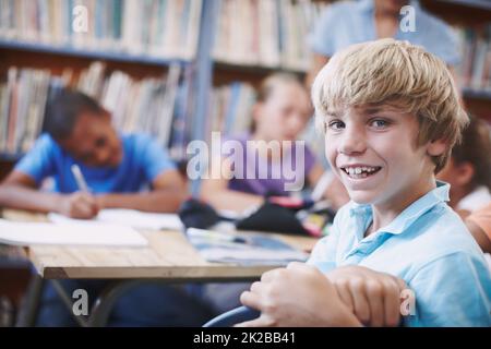 Ich habe so viele Freunde. Ein aufgeregt kleiner Junge, der mit seinen Klassenkameraden in der Bibliothek sitzt. Stockfoto