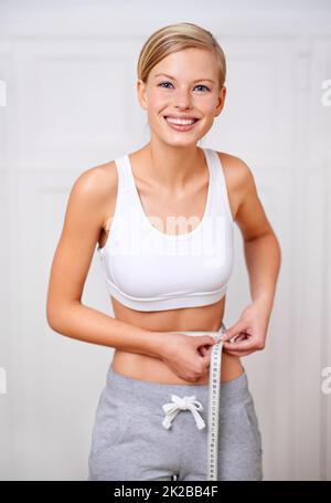 Ich habe mein Zielgewicht erreicht. Ein Porträt einer schönen jungen Frau, die ihre Taille misst. Stockfoto