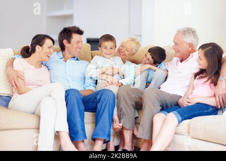 Drei Generationen versammeln sich glücklich zusammen. Drei Generationen Familie sitzen liebevoll auf der Loungecouch zusammen. Stockfoto