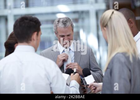 Denken Sie sorgfältig nach, bevor Sie antworten. Aufnahme eines reifen Geschäftsmannes, der seine Krawatte anpasst, während er von Reportern interviewt wurde. Stockfoto