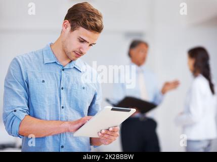 Junger Geschäftsmann, der an einem elektronischen Tablet arbeitet. Porträt eines jungen Geschäftsmanns, der an einem elektronischen Tablet mit Kollegen im Hintergrund arbeitet. Stockfoto