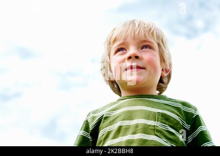 Netter kleiner Junge lächelnd. Blick aus der unteren Perspektive auf einen niedlichen Jungen, der am Himmel steht und lächelt. Stockfoto